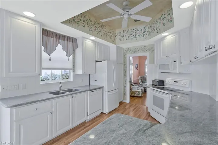 Kitchen featuring white appliances, white cabinetry, light wood-style floors, a tray ceiling, and a sink
