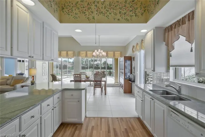 Kitchen with white cabinets, an inviting chandelier, white dishwasher, a sink, and decorative backsplash