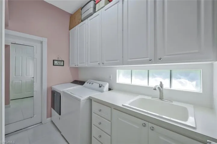 Laundry area with washer and dryer, light tile patterned floors, a sink, and cabinet space