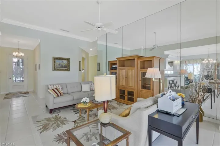 Living area with ornamental molding, tile patterned flooring, visible vents, lofted ceiling, and ceiling fan with notable chandelier