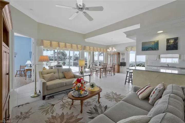 Living room with crown molding, light tile patterned floors, and ceiling fan with notable chandelier