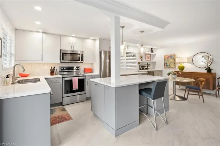 Kitchen with gray cabinetry, stainless steel appliances, hanging light fixtures, a kitchen breakfast bar, and light stone counters