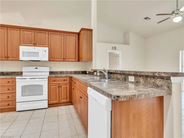 Kitchen featuring white appliances, vaulted ceiling, sink, kitchen peninsula, and light tile patterned floors