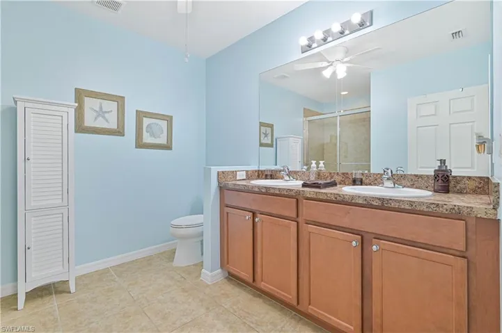 Bathroom featuring tile patterned flooring, toilet, a shower with shower door, ceiling fan, and vanity