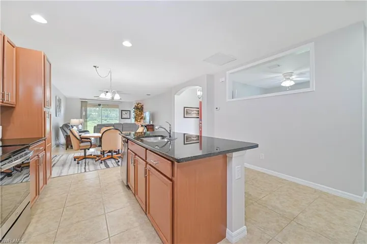 Kitchen with light tile patterned floors, stainless steel appliances, sink, ceiling fan, and a kitchen island with sink