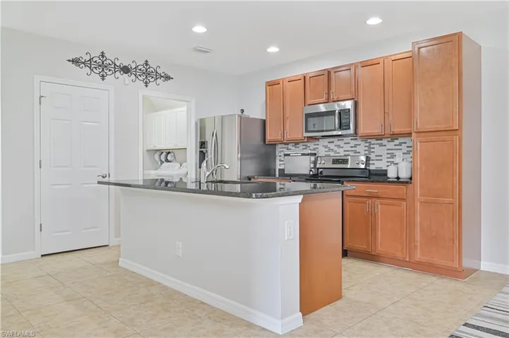 Kitchen featuring backsplash, appliances with stainless steel finishes, sink, light tile patterned flooring, and a kitchen island with sink