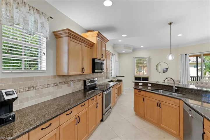 Kitchen with appliances with stainless steel finishes, hanging light fixtures, dark stone countertops, light tile patterned floors, and recessed lighting
