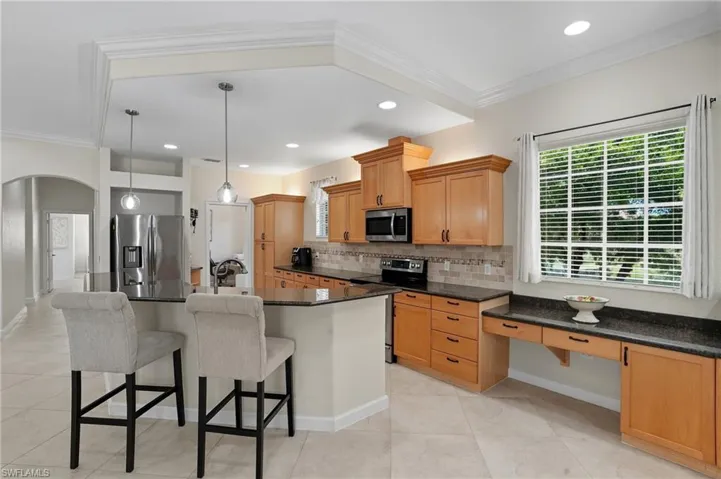 Kitchen featuring crown molding, appliances with stainless steel finishes, a kitchen breakfast bar, backsplash, and a center island with sink