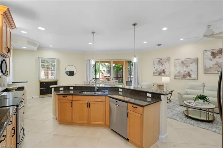Kitchen featuring dark stone countertops, light tile patterned floors, appliances with stainless steel finishes, brown cabinets, and crown molding