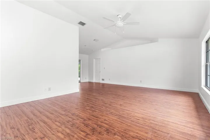 Empty room with vaulted ceiling, a healthy amount of sunlight, ceiling fan, and hardwood / wood-style floors