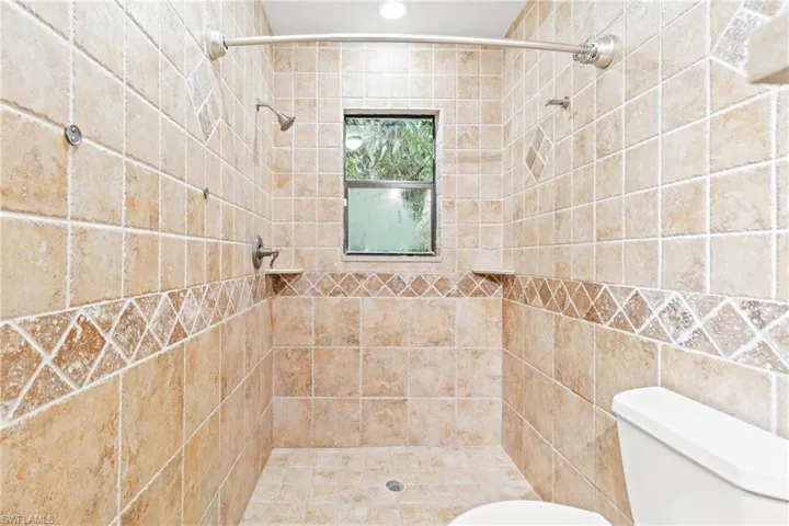 Bathroom with tiled shower, tile walls, and toilet
