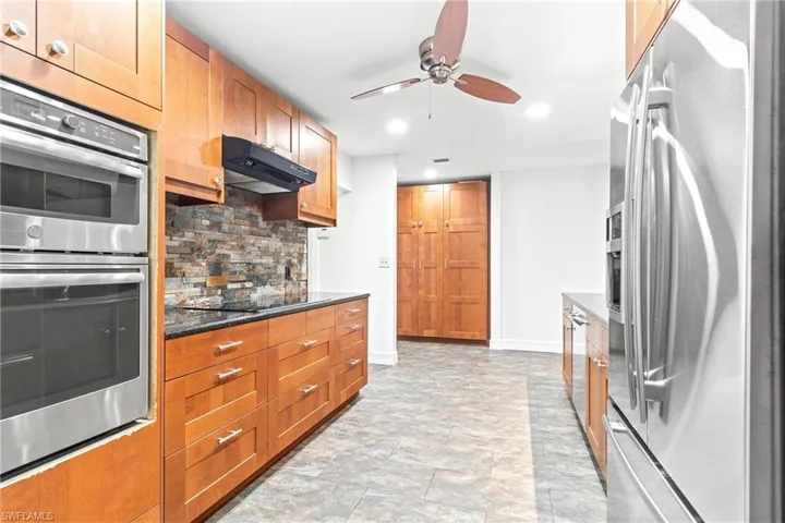 Kitchen with stainless steel appliances, backsplash, light tile patterned floors, dark stone countertops, and ceiling fan