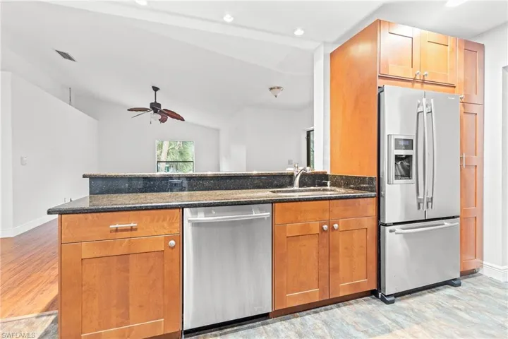 Kitchen with ceiling fan, stainless steel appliances, dark stone countertops, light hardwood / wood-style flooring, and lofted ceiling
