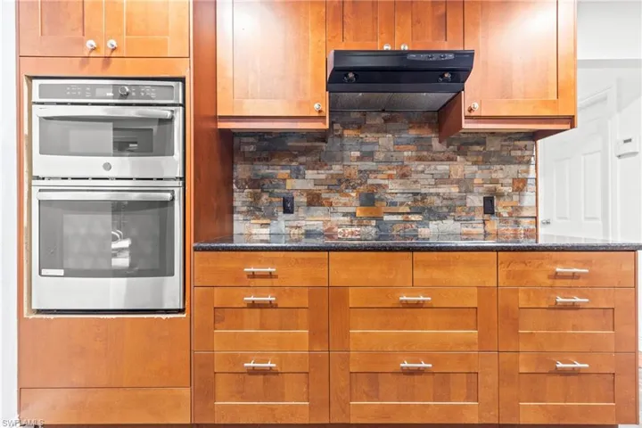 Kitchen featuring extractor fan, tasteful backsplash, black electric cooktop, dark stone countertops, and stainless steel double oven