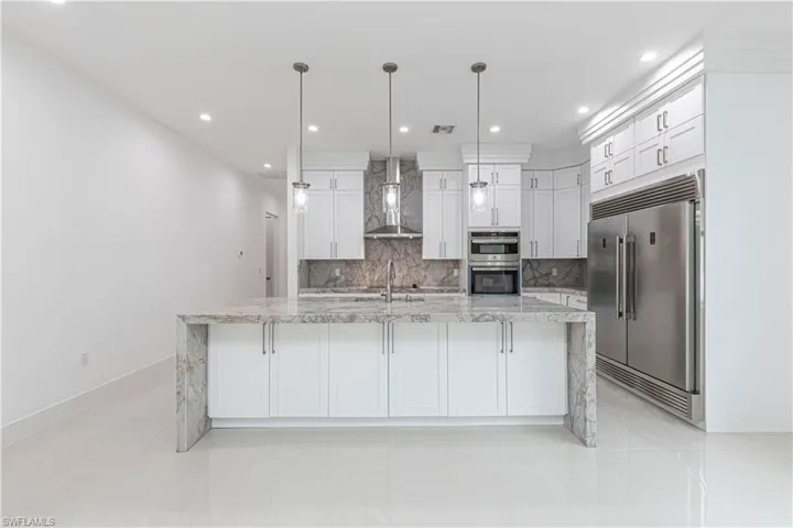 Kitchen with white cabinets, wall chimney exhaust hood, tasteful backsplash, appliances with stainless steel finishes, and a sink