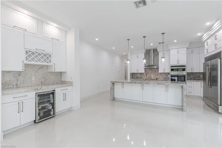 Kitchen featuring white cabinets, visible vents, wine cooler, stainless steel appliances, and wall chimney range hood