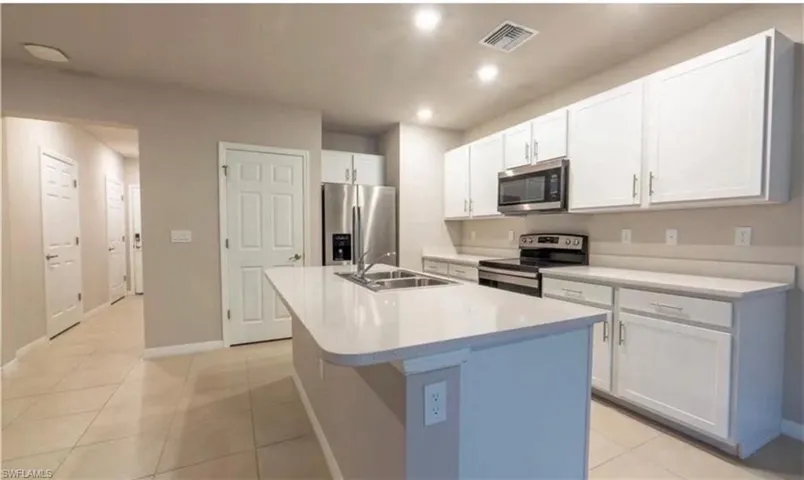 Kitchen featuring stainless steel appliances, white cabinets, light countertops, light tile patterned flooring, and a kitchen island with sink