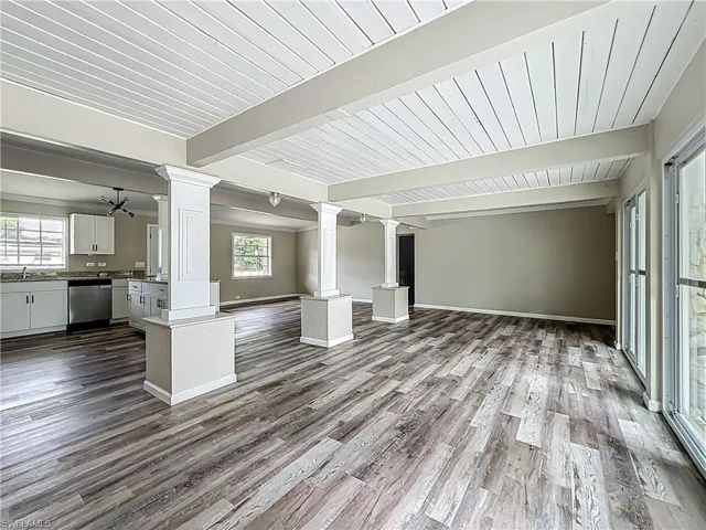 Unfurnished living room with decorative columns, healthy amount of natural light, dark wood-style flooring, and a wood ceiling with exposed beams