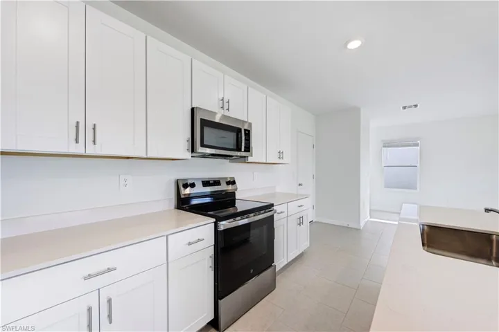 Modern kitchen featuring white shaker-style cabinetry, light-toned countertops, a stainless steel over-the-range microwave, and a black and stainless steel range