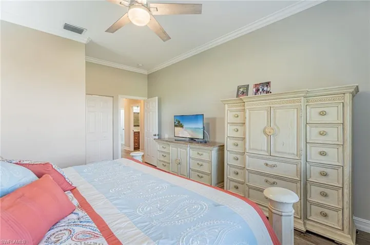Master bedroom crown molding, fan, cabinets, TV and open door into the hall.