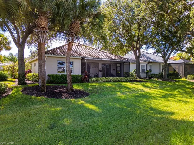 Back of house with lanai, windows, barrel tile roof, various trees, hill, and a beautiful grass.