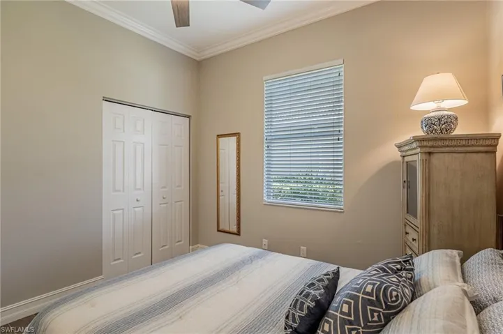 Guest bedroom with fan, crown molding, window, mirror and cabinet.