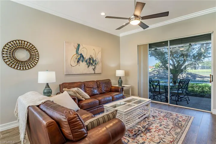 Viewing the living room, the furniture with sliding doors to the lanai, the table outside for relaxing, the oak tree and golf course, make it very nice to enjoy.