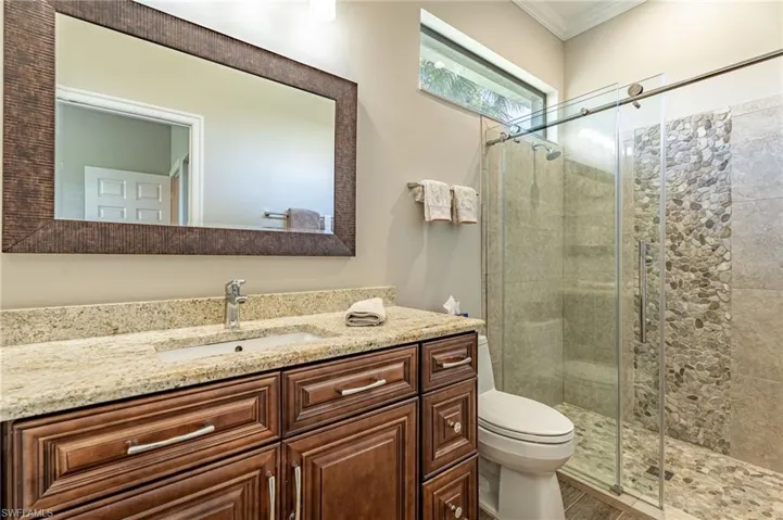 Master bathroom, with cabinets with self closing drawers and doors, granite counter, back splash, Kohler toilets,  mirror with lights on top of the mirror, window, crown molding, shower with rocks on wall and shower floor, sliding glass doors in shower, Porcelain floors.