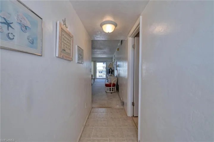 Hallway with light carpet, light tile patterned floors, baseboards, and a textured ceiling
