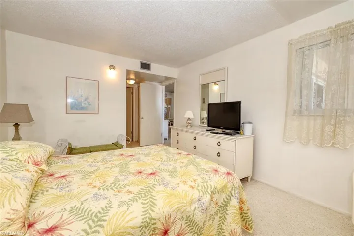 Bedroom with light carpet, visible vents, and a textured ceiling