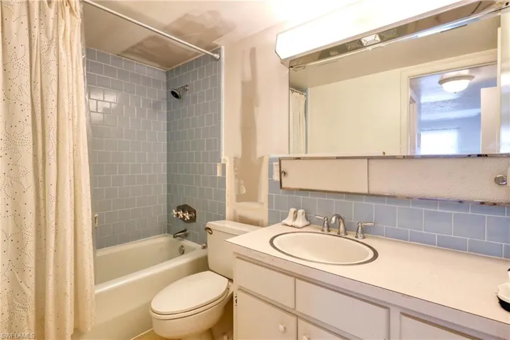 Bathroom with toilet, shower / bath combo with shower curtain, vanity, and tasteful backsplash