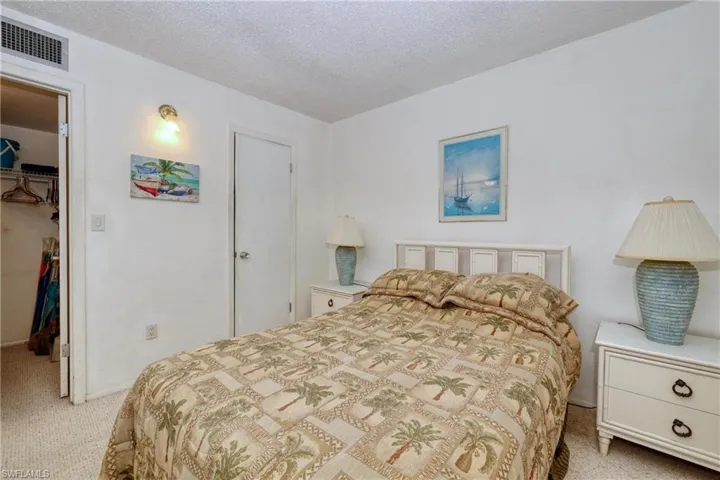 Bedroom featuring visible vents, light carpet, a walk in closet, a textured ceiling, and a closet