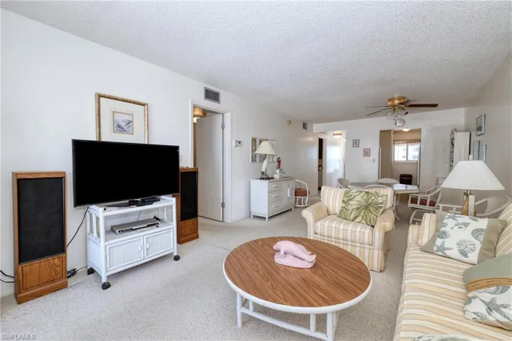 Living room featuring light carpet, visible vents, a textured ceiling, and a ceiling fan