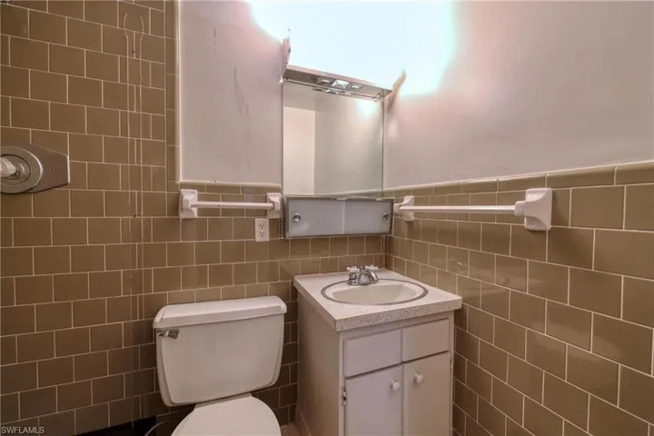 Half bath featuring a wainscoted wall, toilet, tile walls, and vanity