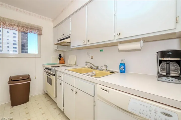 Kitchen with under cabinet range hood, a sink, white cabinetry, white appliances, and light countertops