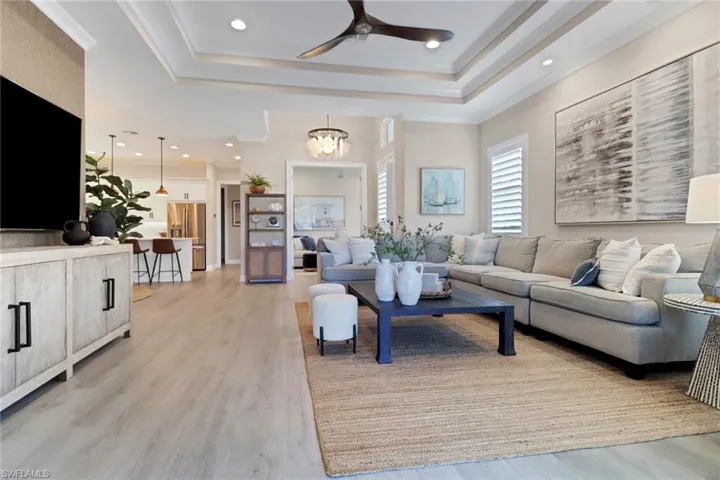 Living area with light wood-type flooring, a raised ceiling, recessed lighting, ceiling fan, and a chandelier