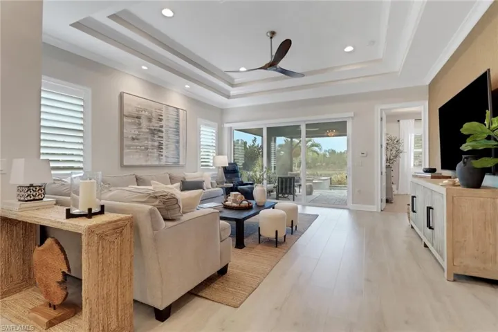 Living room with a raised ceiling, light wood-style floors, a ceiling fan, recessed lighting, and crown molding
