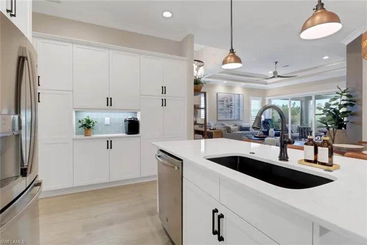 Kitchen featuring hanging light fixtures, appliances with stainless steel finishes, white cabinetry, decorative backsplash, and a raised ceiling