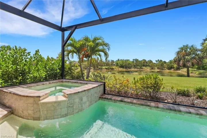 View of pool with a water view, a pool with connected hot tub, a sunroom, glass enclosure, and view of scattered trees