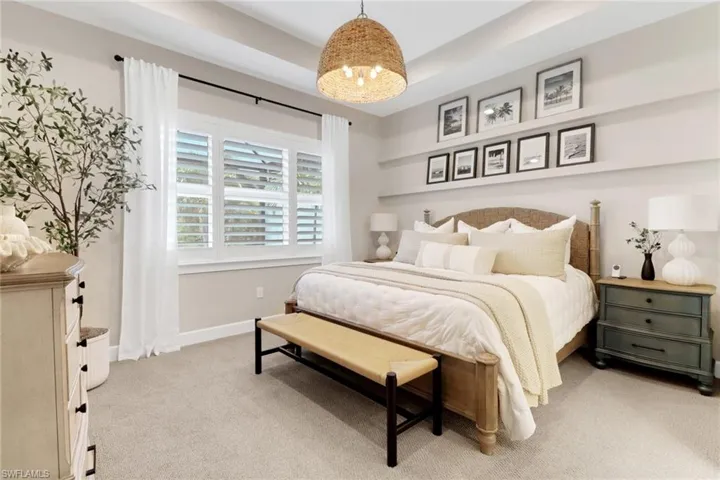 Bedroom featuring light colored carpet, a raised ceiling, and a chandelier