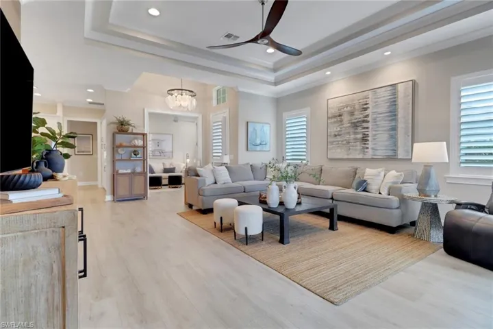Living room with recessed lighting, a ceiling fan, a raised ceiling, light wood finished floors, and a chandelier
