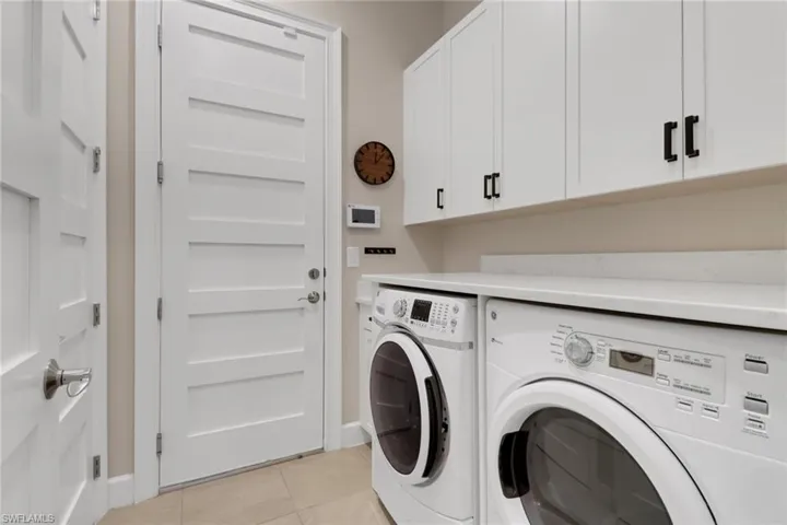 Laundry area featuring light tile patterned floors, cabinet space, and washing machine and dryer