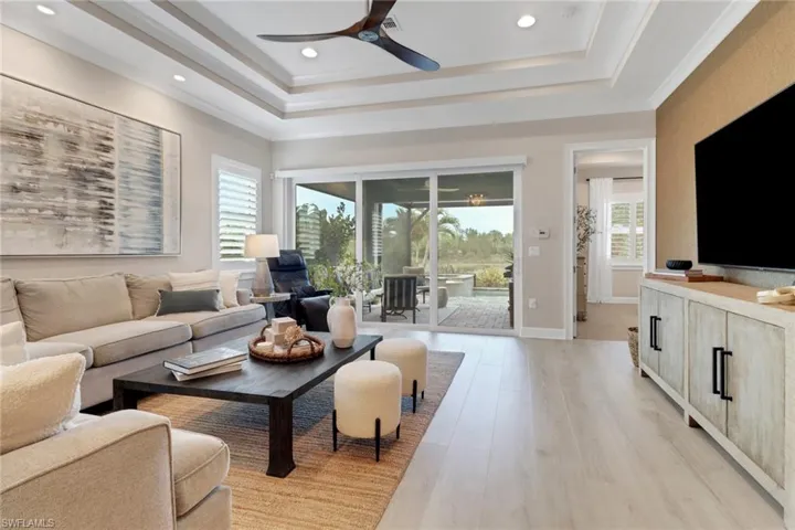Living room with a tray ceiling, light wood-type flooring, recessed lighting, crown molding, and ceiling fan