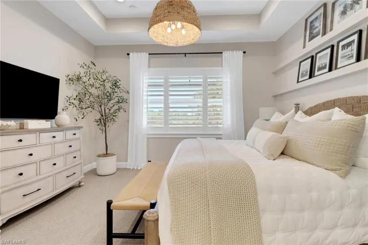 Bedroom with a raised ceiling, light carpet, and a chandelier
