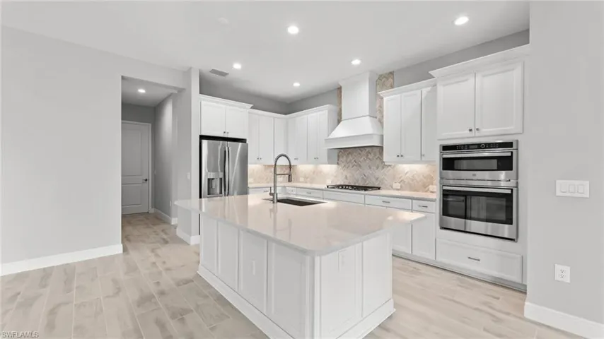 Kitchen featuring light wood-type flooring, custom range hood, stainless steel appliances, sink, and tasteful backsplash