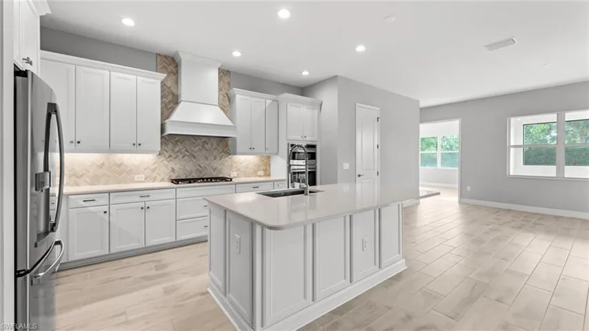 Kitchen featuring a center island with sink, tasteful backsplash, white cabinets, premium range hood, and appliances with stainless steel finishes