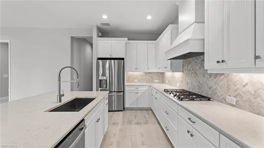 Kitchen featuring light hardwood / wood-style floors, backsplash, appliances with stainless steel finishes, sink, and premium range hood
