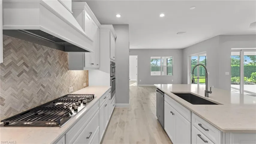Kitchen with custom range hood, stainless steel appliances, white cabinets, sink, and tasteful backsplash