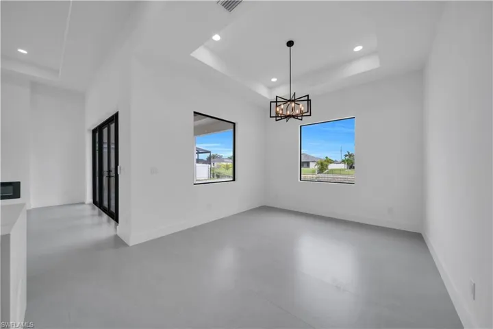 Unfurnished dining area with a raised ceiling, recessed lighting, concrete floors, and a chandelier