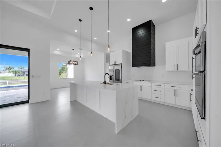 Kitchen with light stone counters, decorative light fixtures, white cabinetry, an island with sink, and recessed lighting